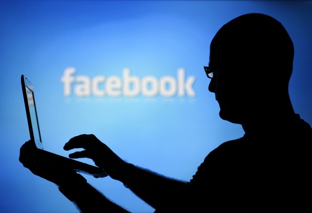 File photo of a man silhouetted against a video screen with an Facebook logo posing with an Dell laptop in this photo illustration taken in the central Bosnian town of Zenica